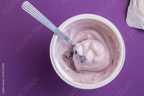 Yogurt cup with blue berry yoghurt, spoon and foil lid isolated on purple background