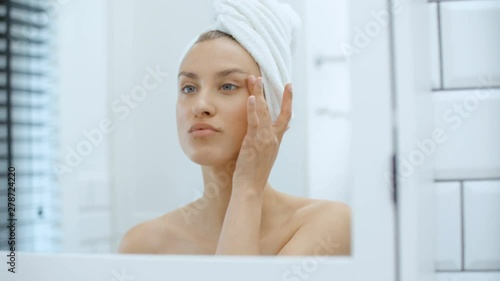 Closeup of beautiful young woman examining herself in front of mirror.