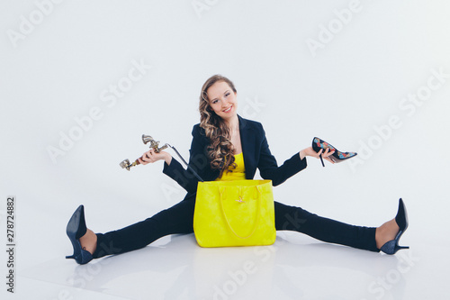 a happy businesswoman in a black and yellow suit takes out a phone and a Shoe from a yellow bag. Beautiful woman sitting on floor on white background