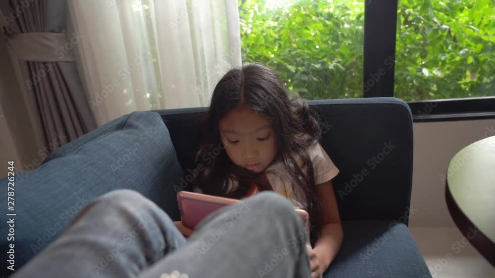 Asian kid girl sitting relax and using tablet computer at home, slow-motion handheld panning high-angle shot Asian kid girl sitting relax and using tablet computer at home, slow-motion handheld panning high-angle shot