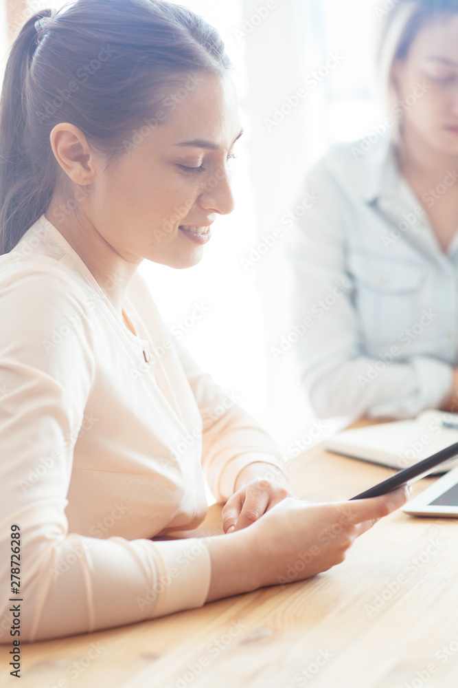 The girl at a business meeting with another girl looks into the phone and smiles The girl at a business meeting with another girl looks into the phone and smiles