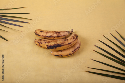 Fototapeta Naklejka Na Ścianę i Meble -  Ugly bananas lie on a yellow background with palm leaves