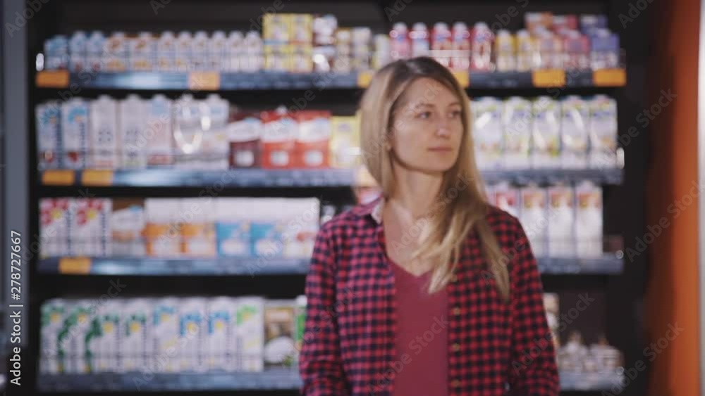 Young modern woman is standing and thinking what food she want to buy and cook for dinner. Shopping chose is everyday complicated question. Retail shelf and fridge are near looking alone female Young modern woman is standing and thinking what food she want to buy and cook for dinner. Shopping chose is everyday complicated question. Retail shelf and fridge are near looking alone female