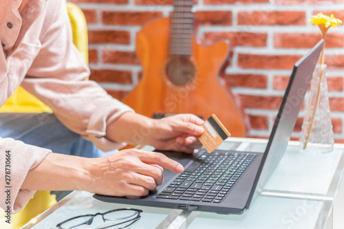 man holding credit card and using laptop computer in living room. online shopping concept