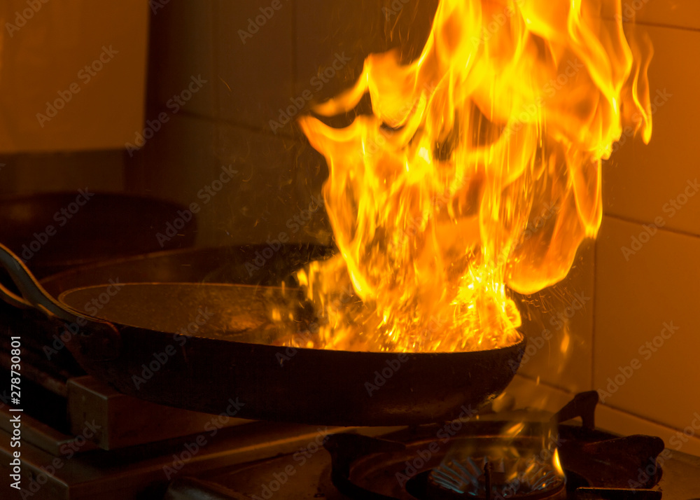 Chef cooking and doing flambe on food in a restaurant kitchen. Close up Chef cooking and doing flambe on food in a restaurant kitchen. Close up