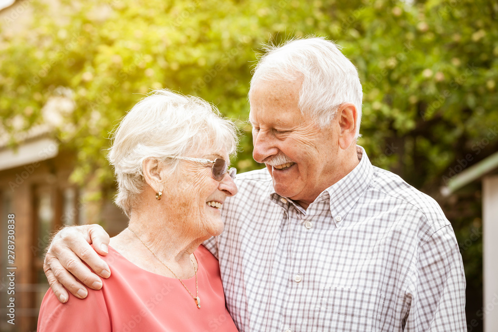 Smart older couple are standing in the garden, hugging each other and laughing at each other Smart older couple are standing in the garden, hugging each other and laughing at each other