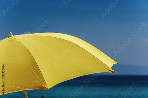 Yellow beach sun umbrella against blue sky. Day sunny view of large open sun blocking intense yellow shade umbrella before summer sea and sky background.