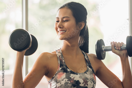 Attractive young sports asian woman lifting weight in gym.