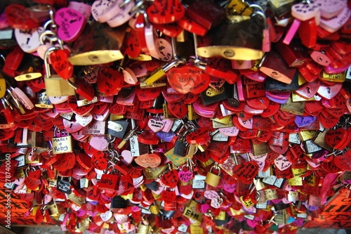 Locked locks of love and loyalty. Wall full of red and pink love locks shaped as hearts and classical locks with writings on each lock,