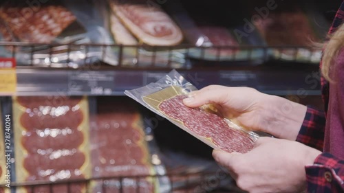 Adult or mature housewife woman wearing in casual stylish clothes buying items in small store near her house. Confident woman holding in her hands package of fresh and sliced salami