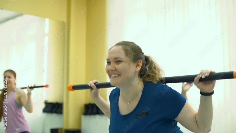Smiling Plump Woman Doing Exercises with Barbell in a Fitness Studio in Slow Motion. Fitness, Sport, Training, Weight Loss, Teamwork and Lifestyle Concept Smiling Plump Woman Doing Exercises with Barbell in a Fitness Studio in Slow Motion. Fitness, Sport, Training, Weight Loss, Teamwork and Lifestyle Concept