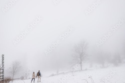Back view on the Caucasian young couple in love walking the hills in the beautiful winter in the coutryside. Rear. Outdoor.