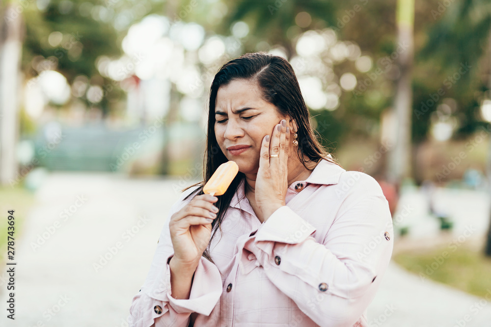 Woman with hypersensitive tooth eating popsicle outdoors Woman with hypersensitive tooth eating popsicle outdoors
