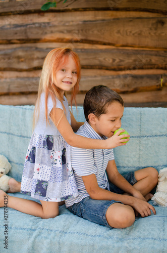 A five-year-old blonde girl feeds her nine-year-old brother with green apples. Happy caucasian children in the garden
