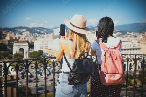 Europe travel summer tourism holiday vacation background - two girls friend with hat mobile cell phone and using backpack in hand taking selfie photo and filming blog