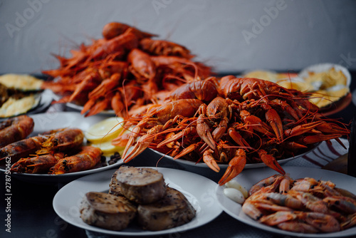 two large plates with boiled crayfish, a plate with fried tuna steak, boiled shrimps and fried lobster