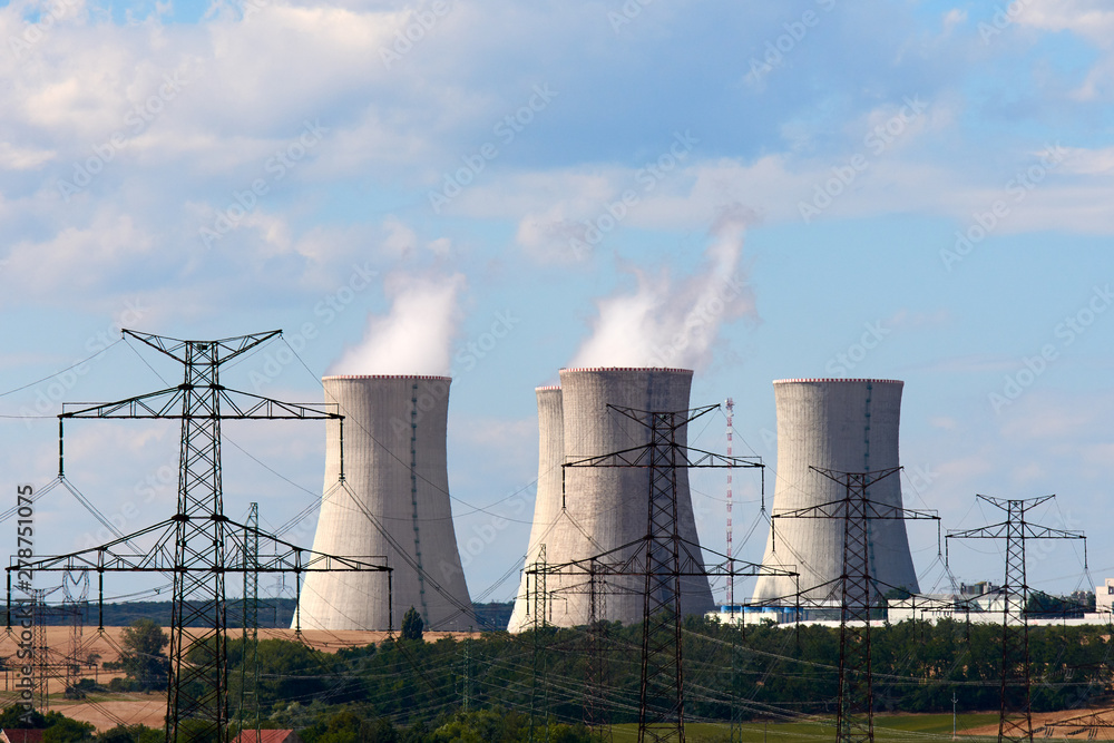 View of smoking chimneys of nuclear power plant, power lines and forest, under blue sky with clouds View of smoking chimneys of nuclear power plant, power lines and forest, under blue sky with clouds