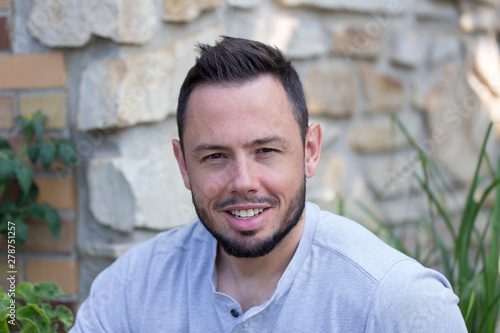 Horizontal closeup of handsome smiling clean cut young man with short beard staring intently against soft focus home background