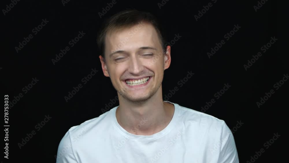 Handsome young man in t-shirt smiling while standing against black background. Male laughs from ear to ear, giggles on the funny stories. False or fake smile Handsome young man in t-shirt smiling while standing against black background. Male laughs from ear to ear, giggles on the funny stories. False or fake smile