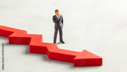 Figurine of a businessman in a suit and tie and a red down arrow. The concept of bankruptcy, falling profits and reducing indicators, analysis of losses