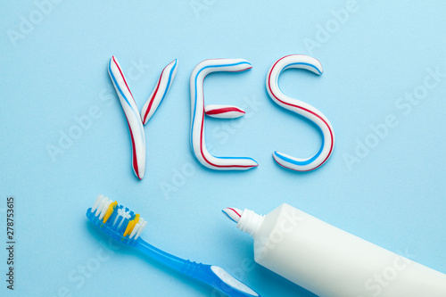 Word YES from toothpaste. Tube of colored toothpaste and toothbrush on blue background. The concept of proper cleaning and care of teeth.