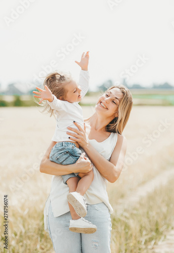 Mother holding a little smiling girl at the wheat field.