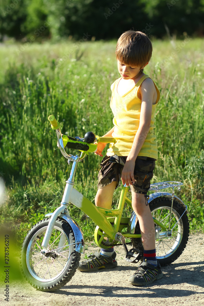 Candid portrait of an upset boy with a bicycle in the sunlit summer field Candid portrait of an upset boy with a bicycle in the sunlit summer field