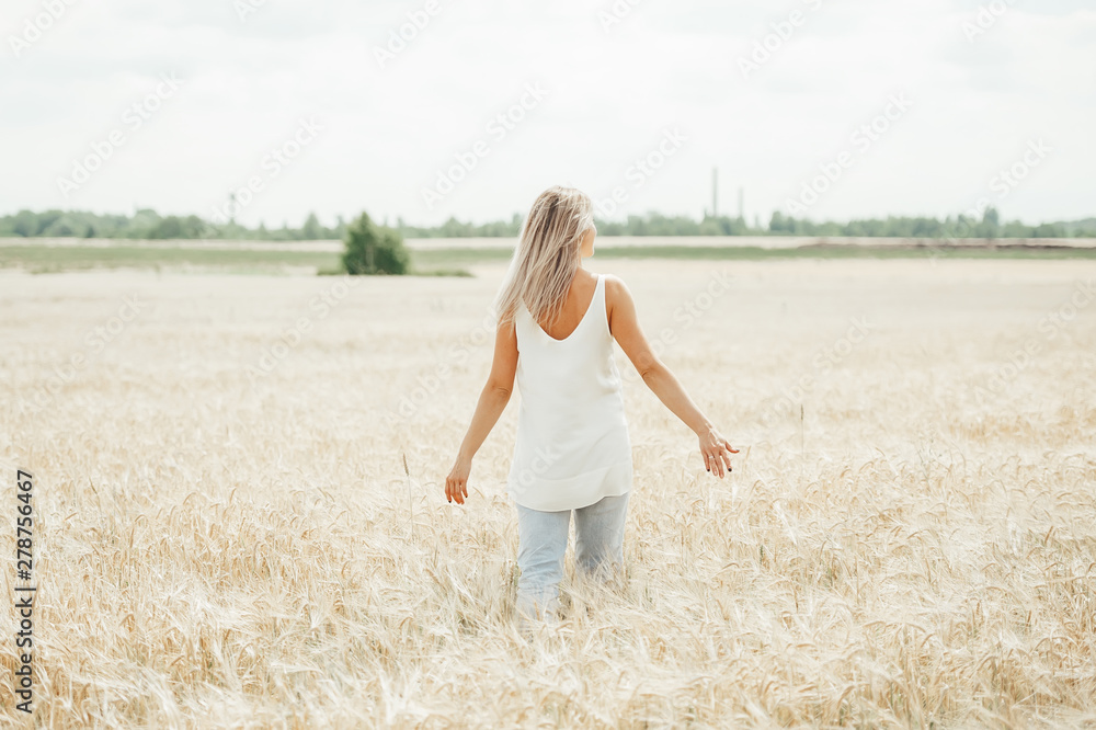 Young woman walking in the wheat field. Back view Young woman walking in the wheat field. Back view