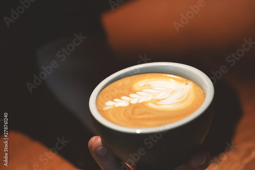 cappuccino cup with coffee milk design in man's hands close up
