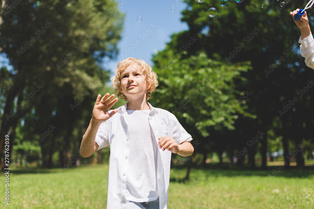 Fototapeta premium adorable boy in white Gesturing near soap bubbles in park