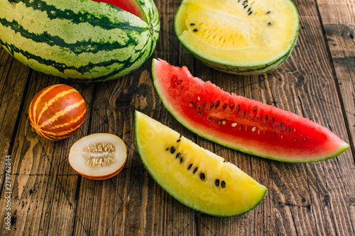 Different watermelons and melon, yellow and red on a wooden background