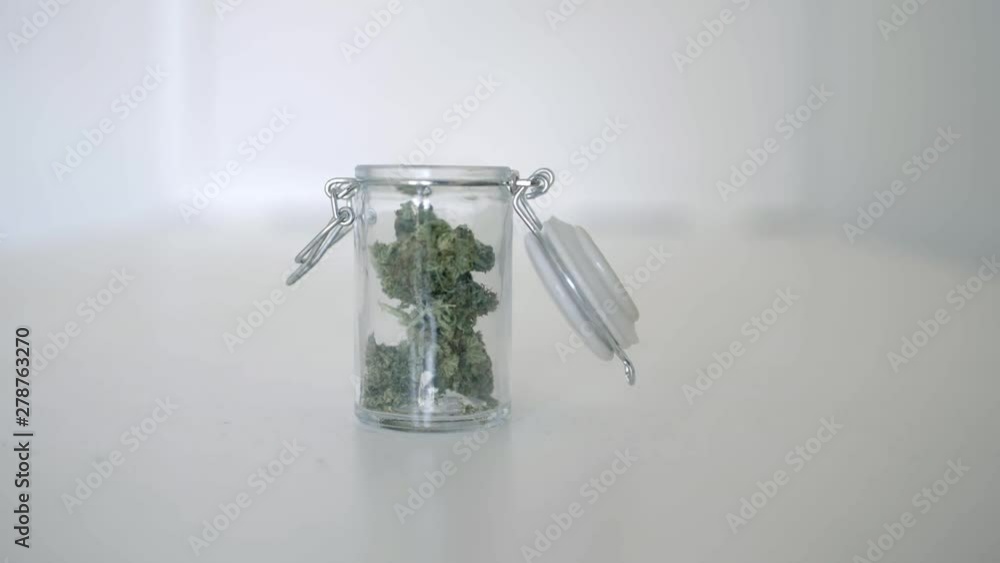 Placing a jar of marijuana on a table a using tweasers to remove some Placing a jar of marijuana on a table a using tweasers to remove some
