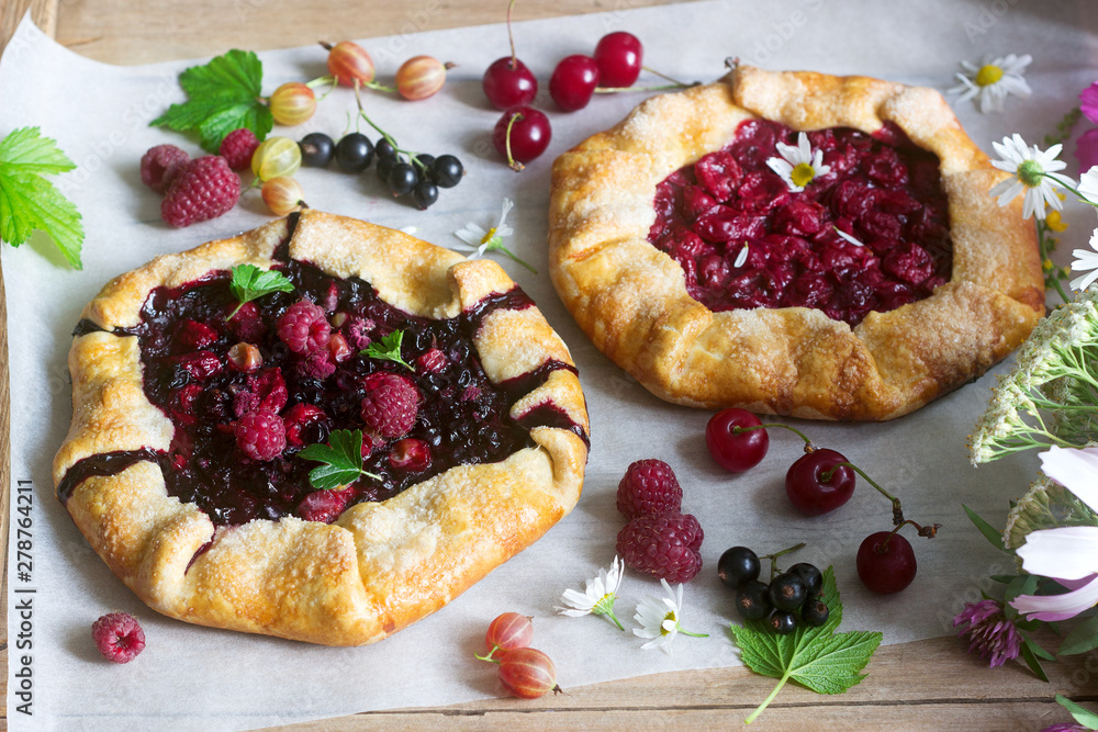 Galette pies with juicy berry filling, berries and wild flowers on a wooden background. Rustic style. Galette pies with juicy berry filling, berries and wild flowers on a wooden background. Rustic style.