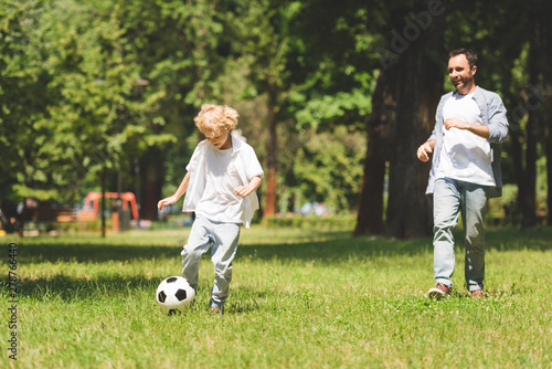 father and adorable son playing football in park during daytime