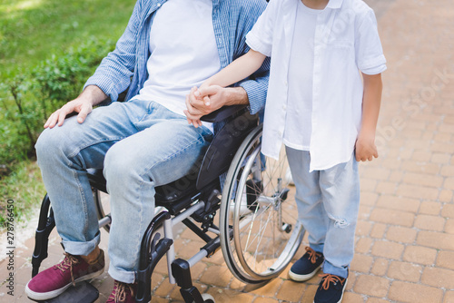 cropped view of son hloding hands with disabled father in wheelchair