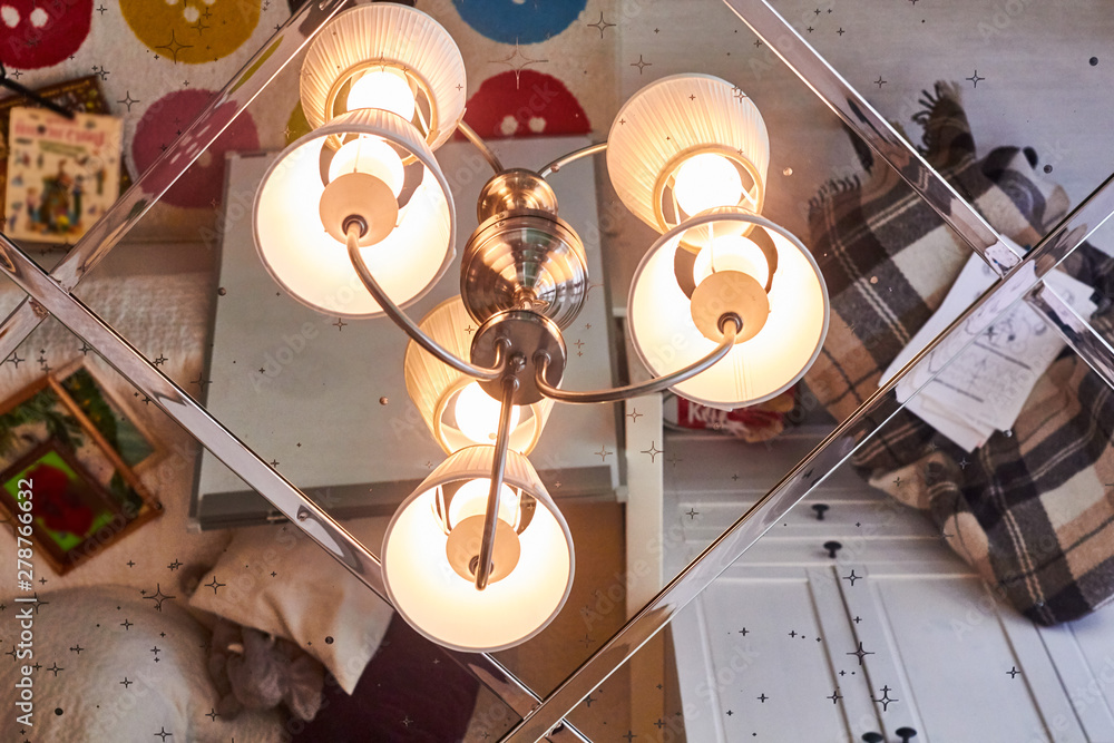 Mirrored ceiling in the bedroom. Chandelier with three lamps close-up. Interior of the living room is reflected in the ceiling mirror. Mirrored ceiling in the bedroom. Chandelier with three lamps close-up. Interior of the living room is reflected in the ceiling mirror.