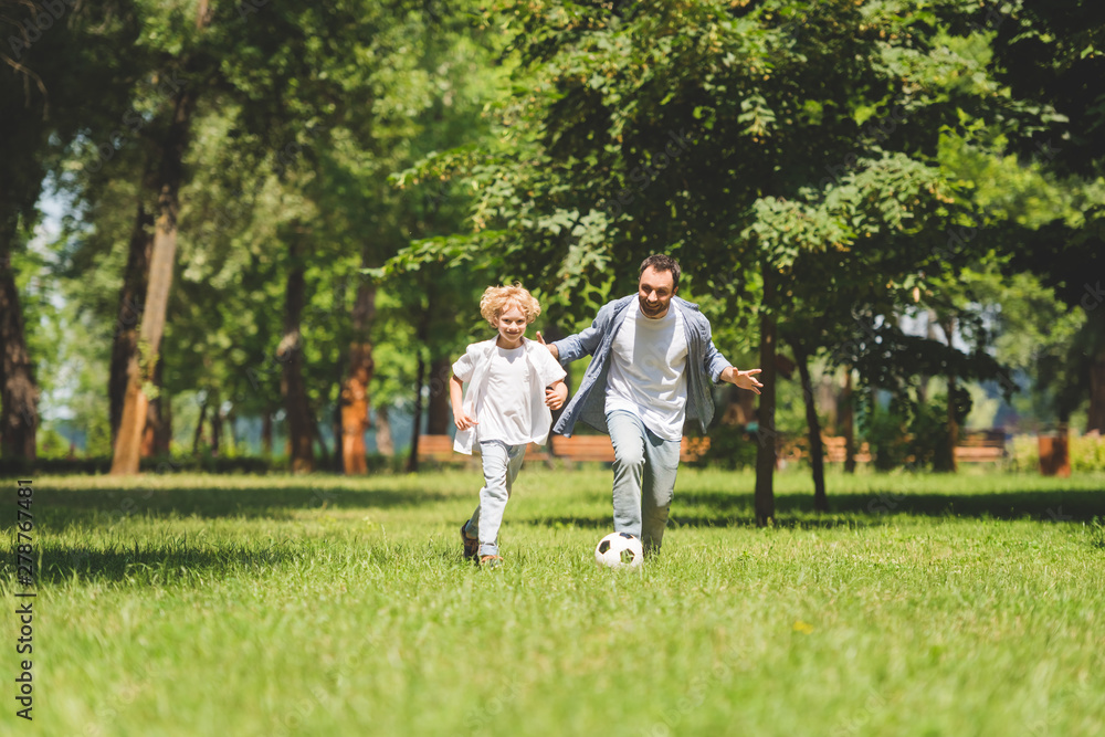 father and adorable son playing football with soccer ball in park father and adorable son playing football with soccer ball in park
