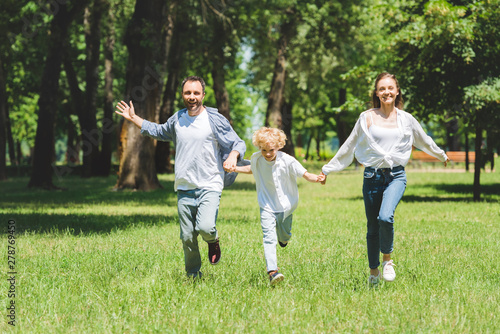 happy family holding hands and running in park during daytime