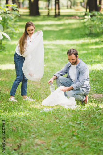 man and woman picking up garbage in plastic bags in park