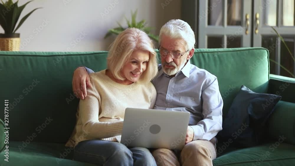 Happy senior couple talking embracing using laptop together at home Happy senior couple talking embracing using laptop together at home