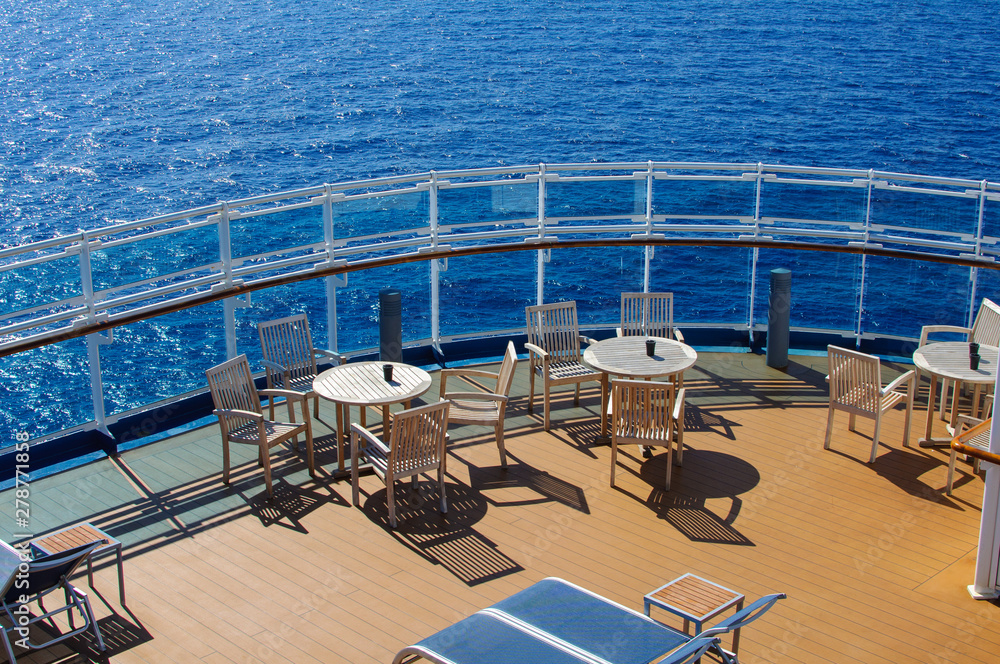 Obraz premium White dining tables with chairs and sun loungers on the deck of the ship against the blue ocean in Sunny weather.