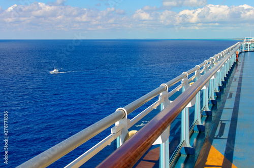 Going into the distance in the perspective of the railing of the deck of the ship on the background of the blue ocean and a white motor yacht on the waves.