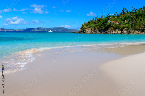 Azure water and white sand of a tropical beach against a green Cape and mountains on the horizon.