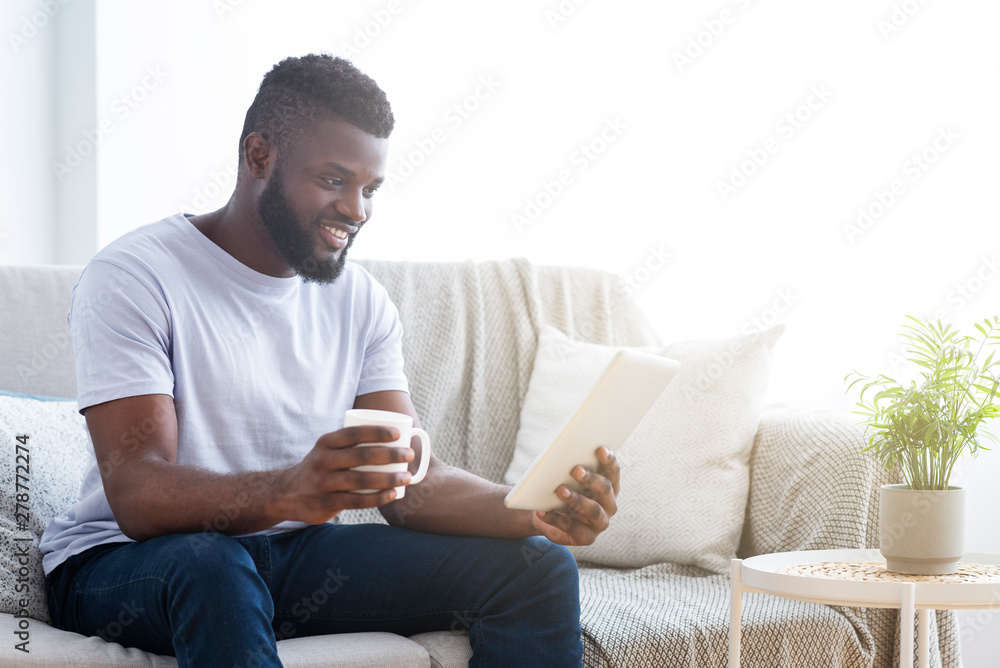 Millennial african-american guy reading digital tablet and enjoying coffee Millennial african-american guy reading digital tablet and enjoying coffee