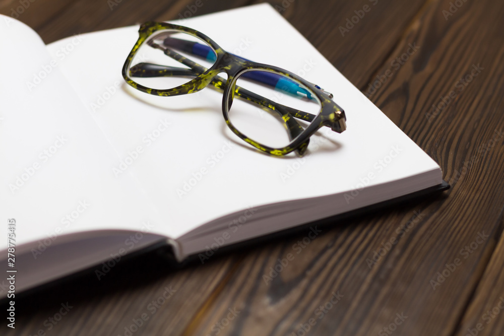 Open blank book, pen and glasses on dark wooden table. View from above. Space for text. closedup Open blank book, pen and glasses on dark wooden table. View from above. Space for text. closedup