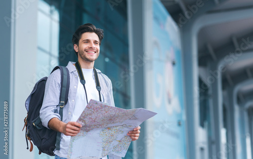 Cheerful man traveler holding map, studying new destinations at airport photo