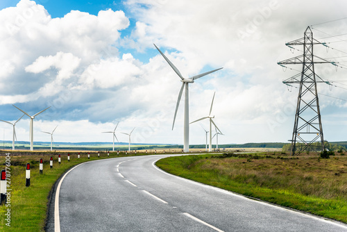 Winding road running through wind turbines and high voltage pylons