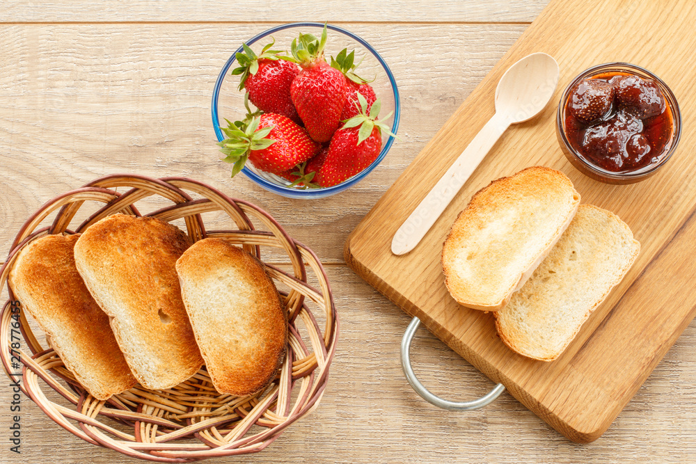 Traditional homemade strawberry jam in bowl, fresh berries with toast on wooden background.