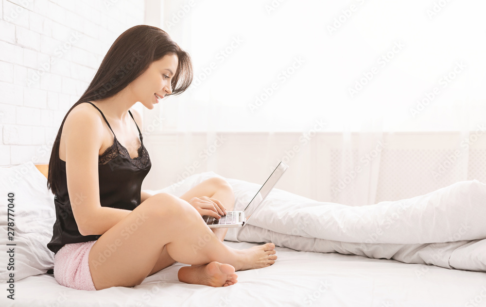 Female blogger typing on laptop in bed Female blogger typing on laptop in bed