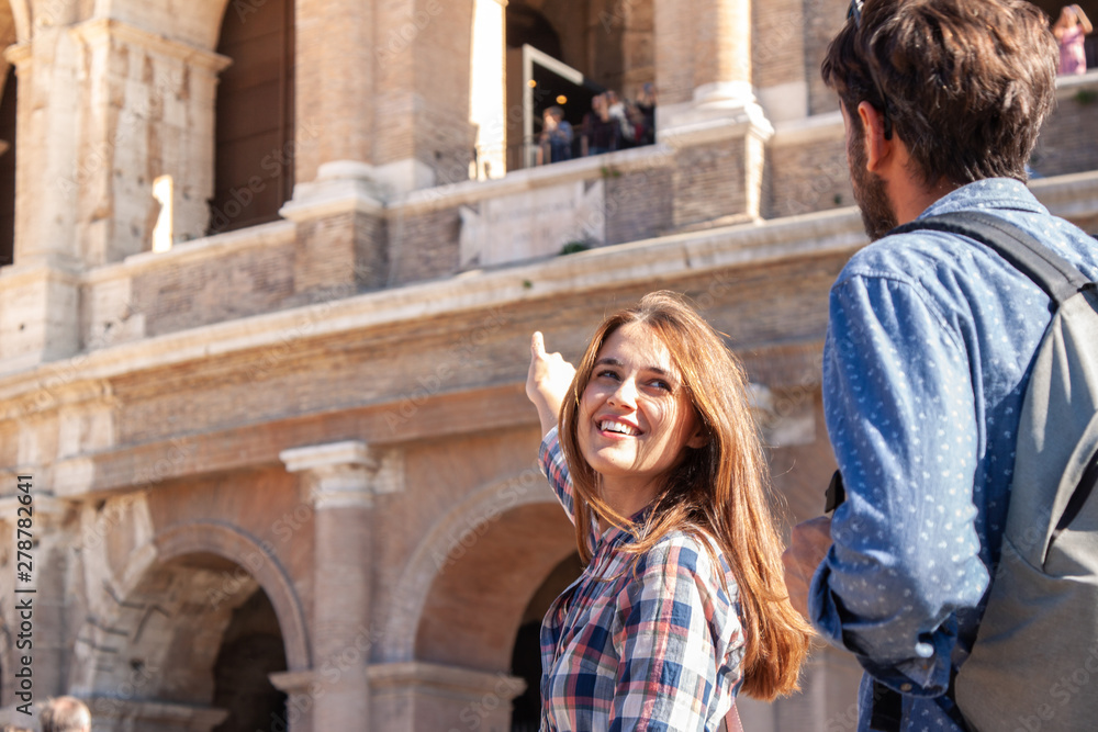 Happy young couple tourists in front of colosseum in rome pointing